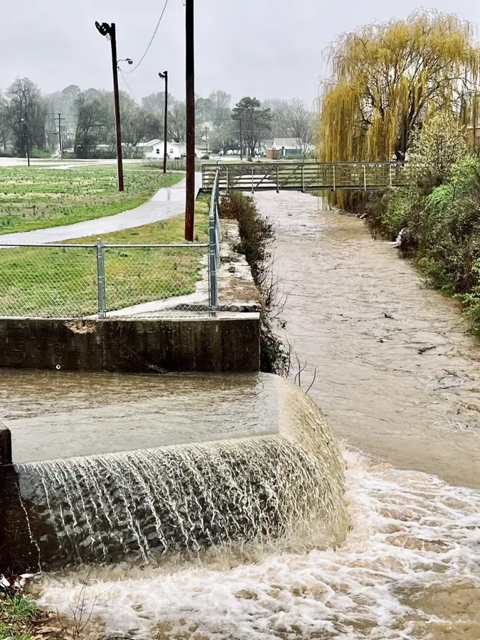 Storm runoff pouring over a weir in a swollen suburban creek channel