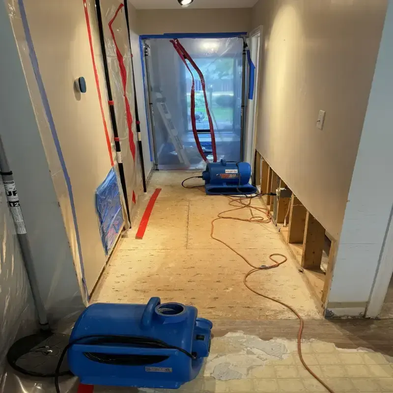 Hallway with the lower drywall cut out, air movers running and plastic containment during a Ballwin dry-out