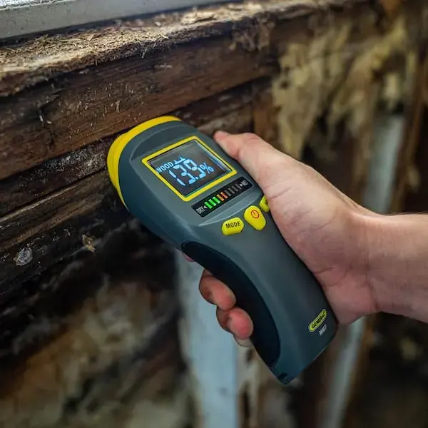 Pin moisture meter reading wet framing during a structural drying check
